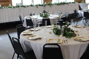 Close up of table decoration at a wedding at the Odessa Center with white tablecloths, greenery and black lantern centerpieces and square wood-style place settings.