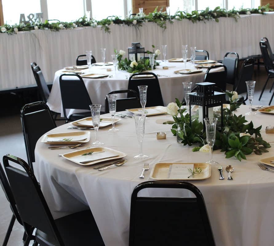 Close up of table decoration at a wedding at the Odessa Center with white tablecloths, greenery and black lantern centerpieces and square wood-style place settings.