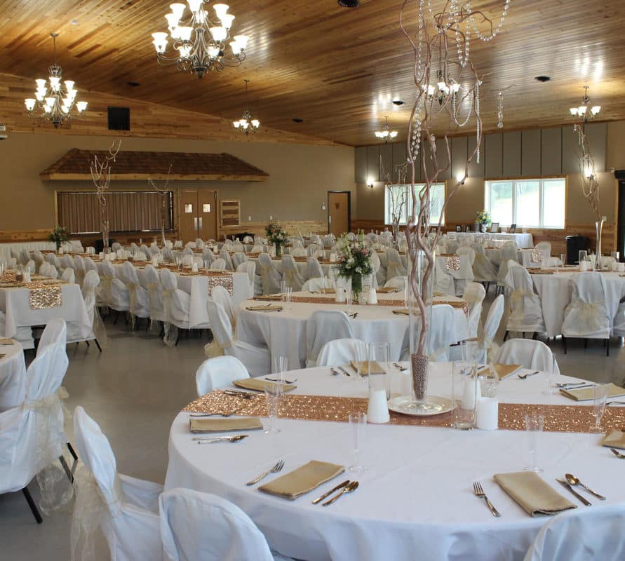 Odessa Event Center decorated with white tablecloths and white chair covers with rose gold accents and centerpieces with tree branches.