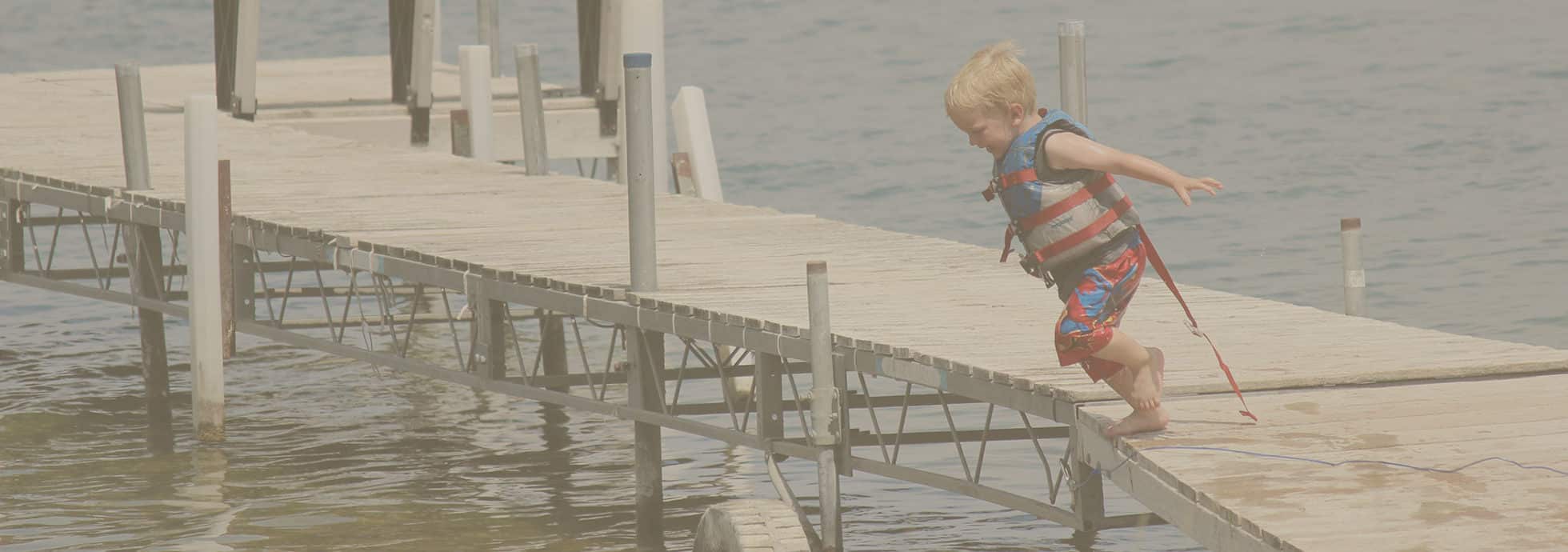 Happy young kid in life vest jumping into water from a boat dock at Eastbay Campground.