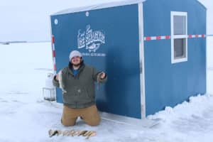 A happy man displays all the fish he caught on the snow outside of an Eastbay Campground Ice House rental.