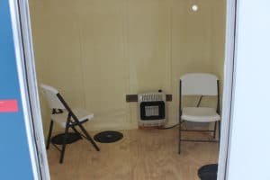 Interior picture of Eastbay Campground ice fishing house with two chairs, a heater, and pre-drilled holes.